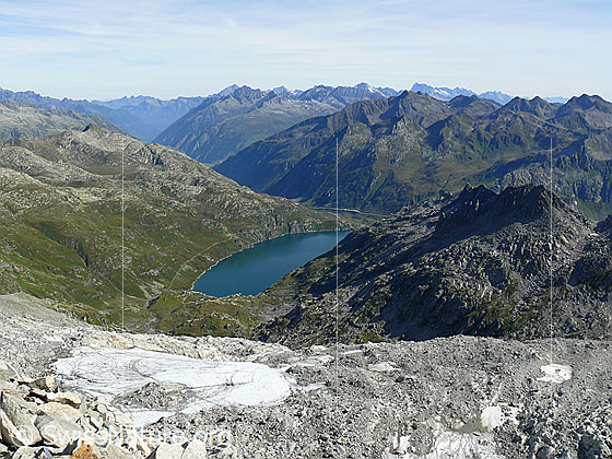 Foto: Tiefblick vom Pizzo Lucendro auf den Lucendrogletscher und den Stausee Lago di Lucendro.
Im Hintergrund sind u.a. Gross Windgällen, Rienzenstock, Gross Ruchen, Oberalpstock, Chastelhorn, Tödi und Pizzo Centrale zu sehen.