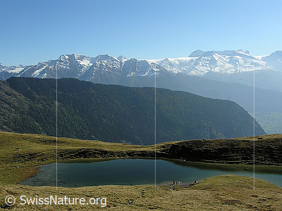 Foto: Lüsgersee und Berglandschaft mit verschneiten Gipfeln und Föhnwalze. Der Bergsee ist von herbstlichen Alpweiden umgeben.
