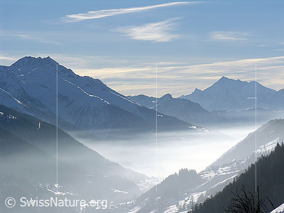 Foto: Dunsstschicht über dem Goms. Bättlihorn und Weisshorn heben sich im Horizont als Silhouetten ab. Am Himmel sind Schleierwolken zu sehen.