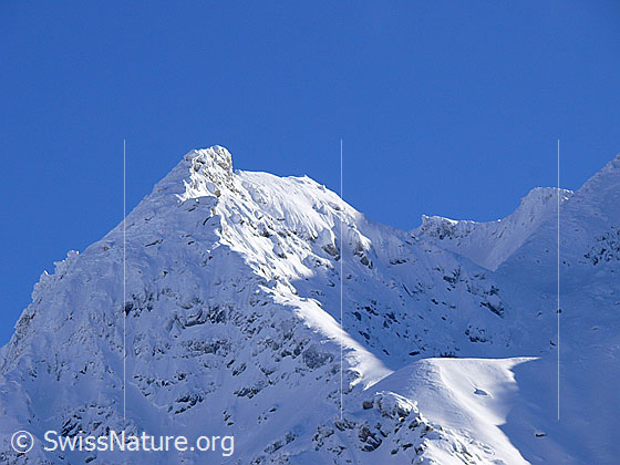 Foto: Stimmung mit Licht und Schatten auf verschneitem Berg (Chollerhorn). Darüber blauer Himmel.