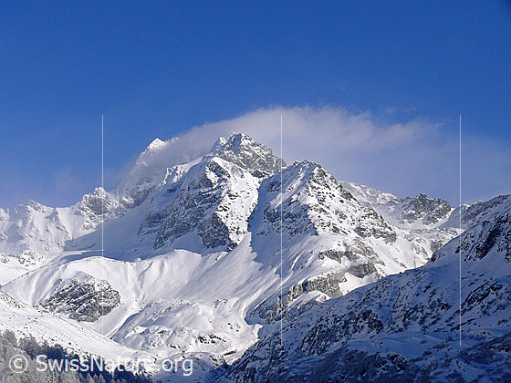 Foto: Frisch verschneite Berglandschaft mit Wolkenfahne im Gipfelbereich des Ofenhorns.