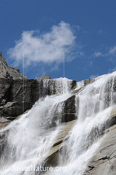 Foto: Mächtiger Wasserfall im Grimselgranit. Das Wasser stürzt sich stiebend über die Felsstufen und fliesst über geneigte Felsplatten.