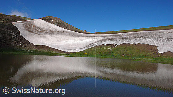 Foto: Formen in der Landschaft. Schneereste unterstreichen die Linien und Rundungen dieser lieblichen Berglandschaft mit Spiegelung im See.