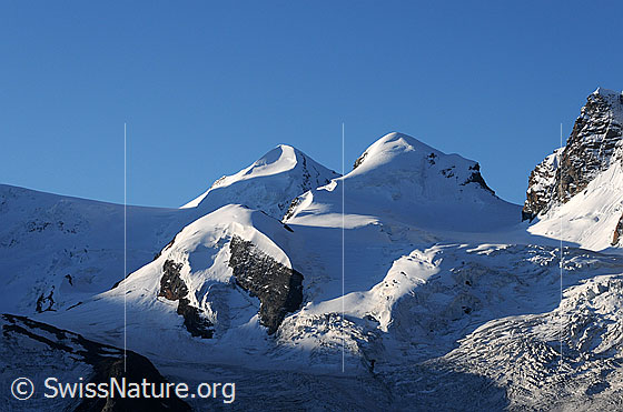 Foto: Castor und Pollux im Morgenlicht. Licht und Schatten fällt auf die Gletscherlandschaft mit den Zwillingen und dem Schwärzegletscher.