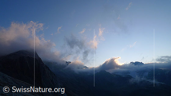 Foto: Morgenstimmung mit leicht gefärbten Wolkenfetzen über der Berglandschaft.