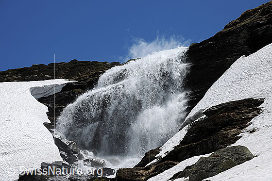 Foto: Wasserfall und Schneereste. Das erfrischende Wasser stürzt sich über eine Felsstufe.
