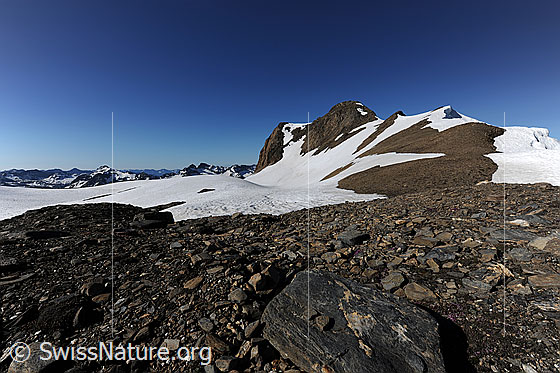 Foto: Natürliche Terrasse aus flachen Steinen und Felsplatten mit Aussicht auf eine Berglandschaft mit schneebedeckter Hochebene und auf das Holzijhorn mit verwächtetem Grat.