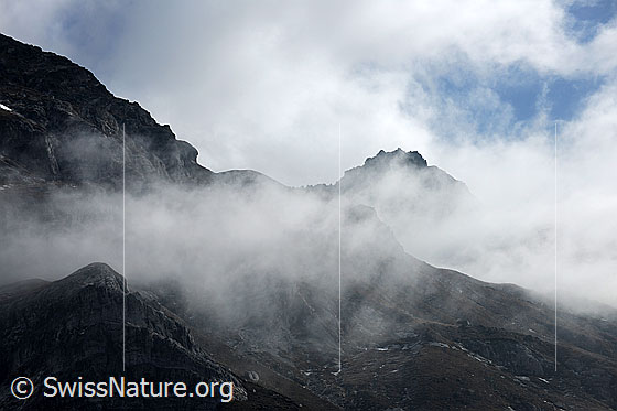 Foto: Nebelstimmung über den Graten einer Berglandschaft. Nebelschwaden und Restbewölkung hüllen die Berge stimmungsvoll ein.