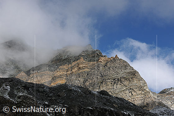 Foto: Wolkenstimmung in den Felsen des Schwarzberg mit Licht und Schatten. In den Felsenwänden sind Felsformationen und bräunliche Felsbänder erkennbar.