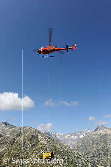 Foto: Helikopter im Einsatz für die Sanierung eines Bergwegs. 
Der am Seil befestigte Kompressor wird umplaziert.