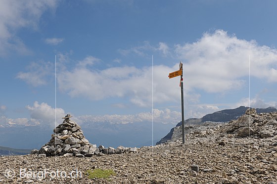 Foto: Schnidejoch.
Am Übergang stehen Steinmann und Wegweiser und über dem Wallis sind Quellwolken zu sehen.